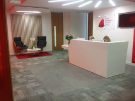 woman sitting behind a white desk in a reception with grey carpets and two chairs in the corner