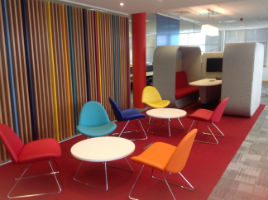 red, orange and blue chairs surrounding a table in an office with red carpet