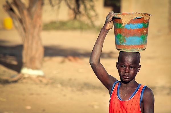 Boy carrying clay in wooden bucket on his head