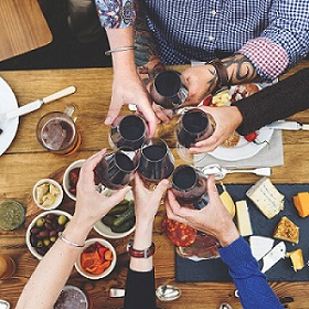 group of people cheering their glasses of wine together over a table of food