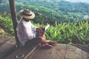 man sitting against pole that overlooks jungle whilst looking at his table