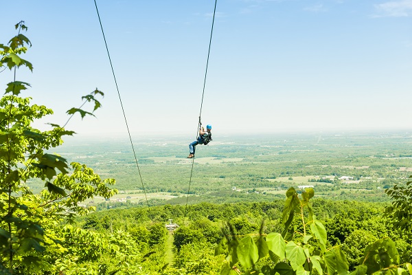 person ziplining down a zipwire over a green forest